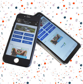 Das Bild zeigt zwei Handys mit dem Startbildschirm der App Emsbüren vor gepunktetem Hintergrund